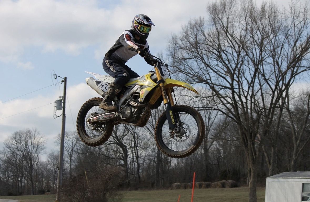 Kolya airborne on his dirt bike against a sky full of clouds.